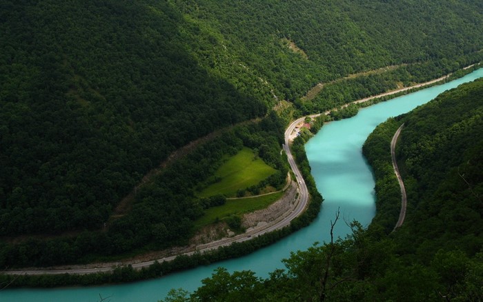 Turquoise river winding through a forested mountain valley with a road