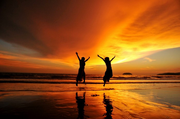 Two people jumping on a beach at sunset