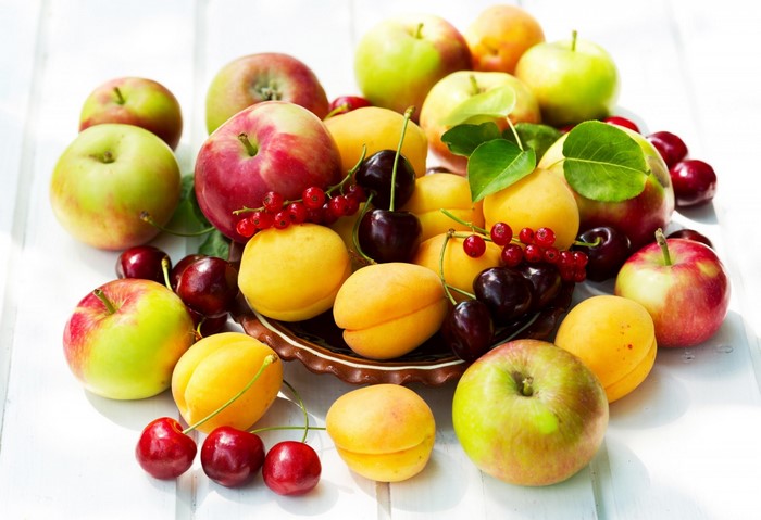 Assortment of fresh fruits including apples, apricots, cherries, and currants