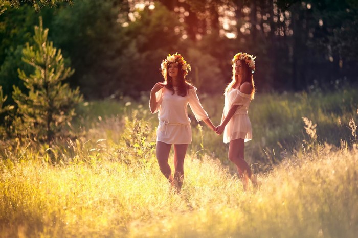 Two women in flower crowns holding hands in a field