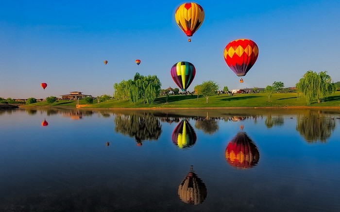 Hot air balloons reflected in a lake at sunrise