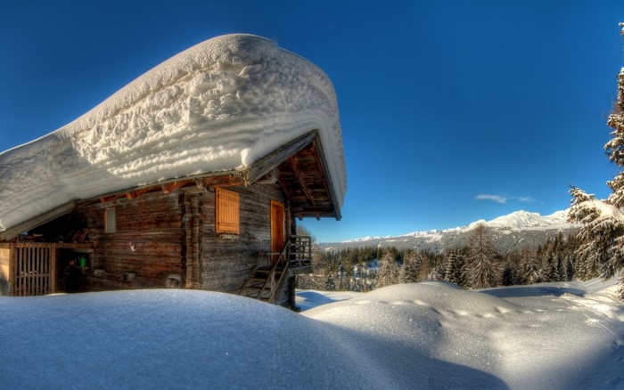 Wooden hut covered in snow with mountains in the background