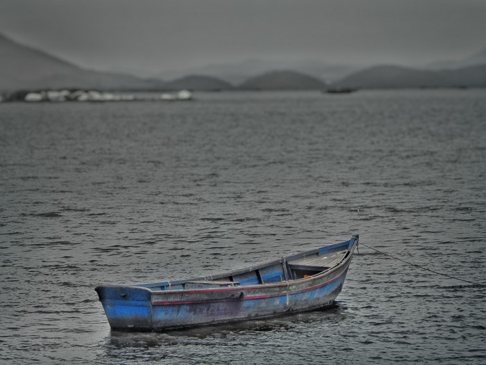 A blue boat floats on the water near a distant shore.