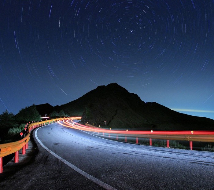 Star trails over a mountain road at night