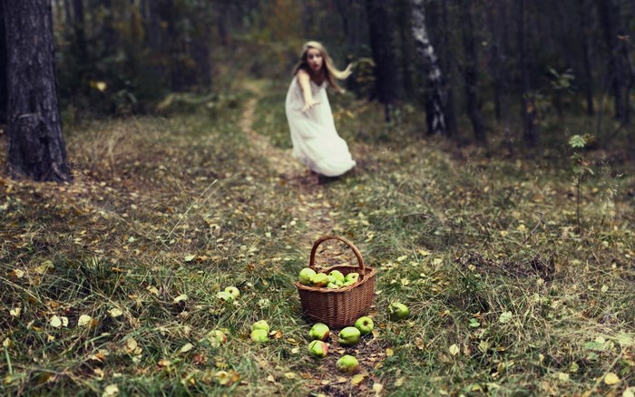 Girl in white dress in forest with basket of apples