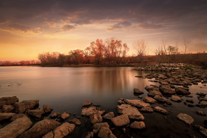 Sunset over a calm lake with trees and rocks