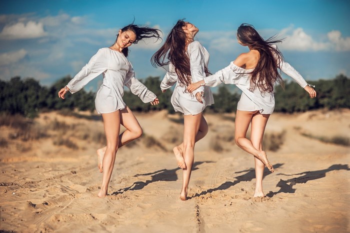 Three women in white dresses dancing on sand
