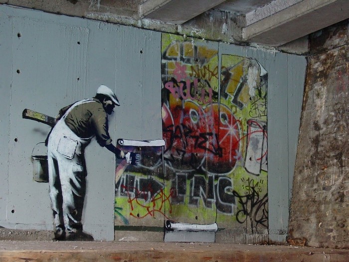 Banksy street art of a painter covering graffiti