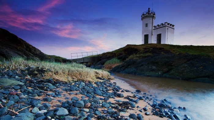 White tower on a rocky shore at dusk with colorful clouds