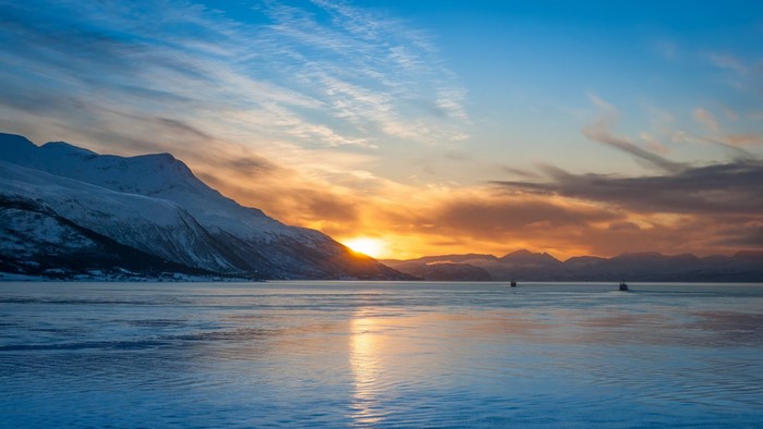 Snowy mountains at sunset over a calm sea