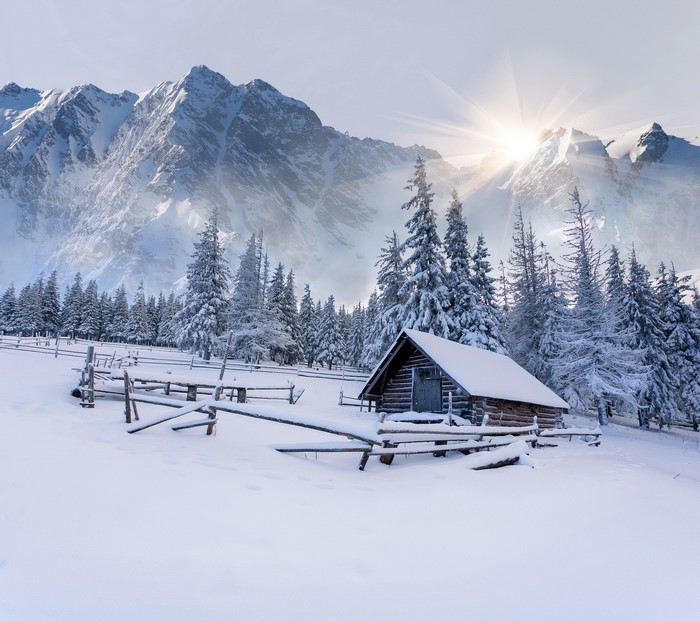 Snowy cabin in the mountains with sun rays