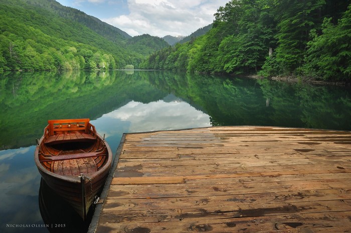 Wooden boat docked on a lake with forested mountains