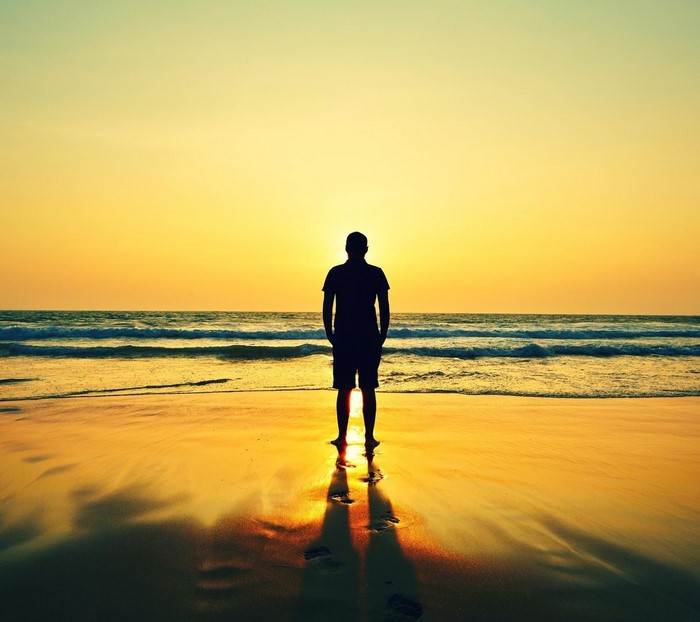 Man silhouetted against sunset on a beach