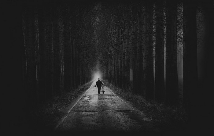 Man walking with bicycle on a dark forest road