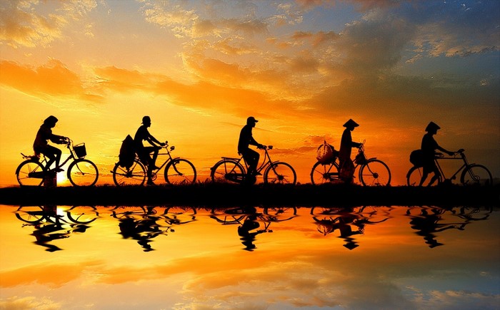 Silhouettes of people riding bicycles at sunset with reflection