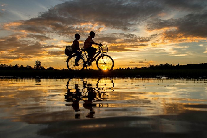 Two children riding a bicycle at sunset with reflection