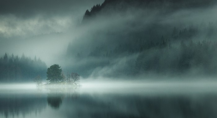 Misty lake with island and forest in Scotland