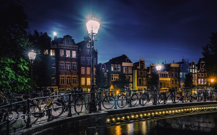 Amsterdam canal bridge at night with bicycles and buildings