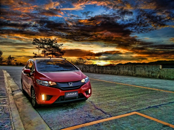 Red Honda Jazz car on road at sunset