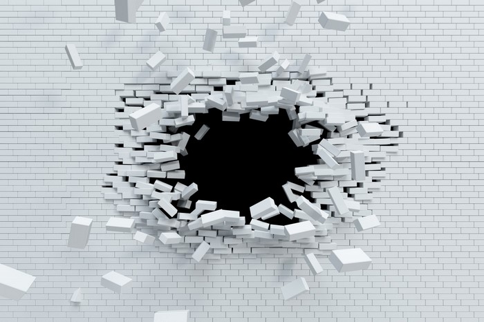 White brick wall breaking apart with debris flying