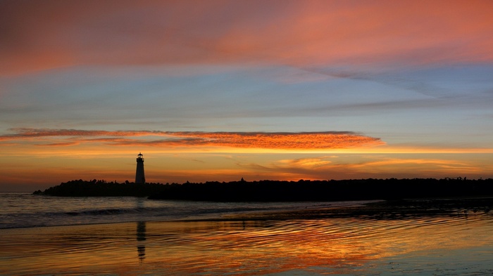 Lighthouse silhouetted against a colorful sunset over the ocean