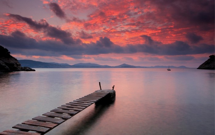 Wooden pier at sunset over the sea with a sailboat