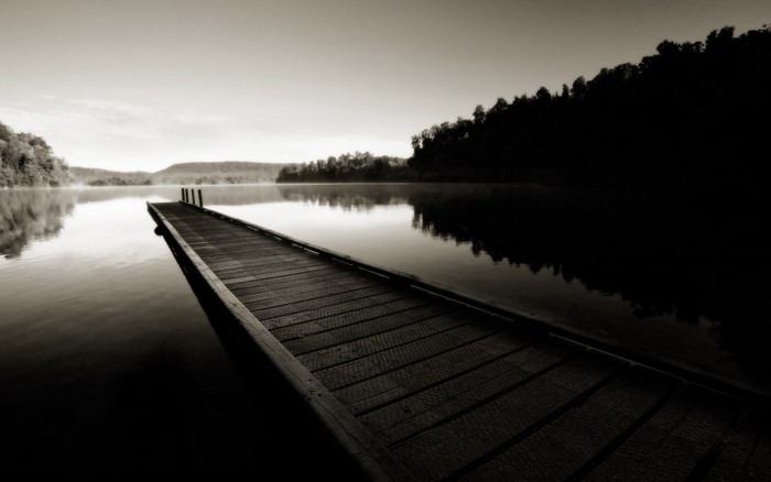 Monochrome image of a wooden dock on a misty lake at dawn