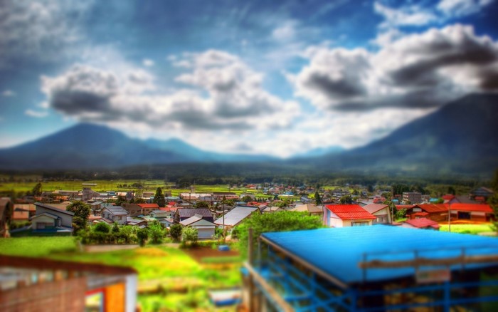 Tilt-shift photography of a rural town with mountains in the background