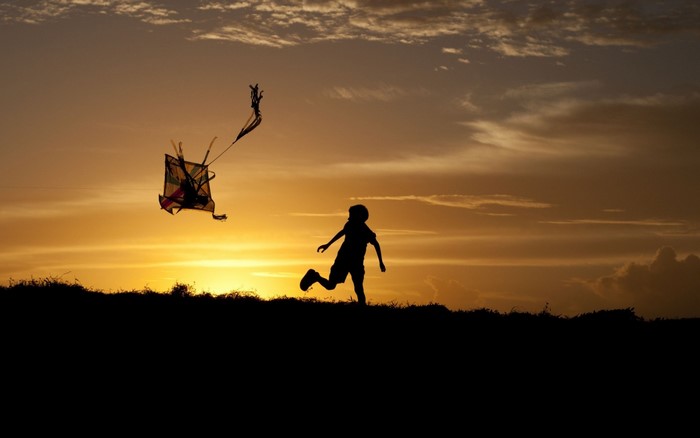 Silhouette of a child flying a kite at sunset