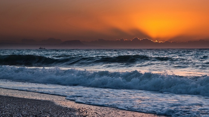 Sunset over the ocean with waves crashing on the shore