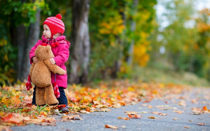 Child holding teddy bear in autumn park
