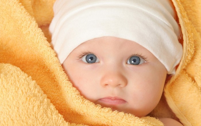 Baby wrapped in a yellow towel wearing a white hat
