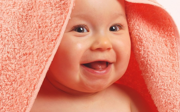 Close up of a smiling baby wrapped in a pink towel
