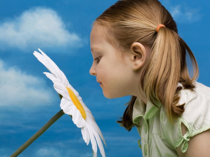 Girl smelling a large daisy against a blue sky