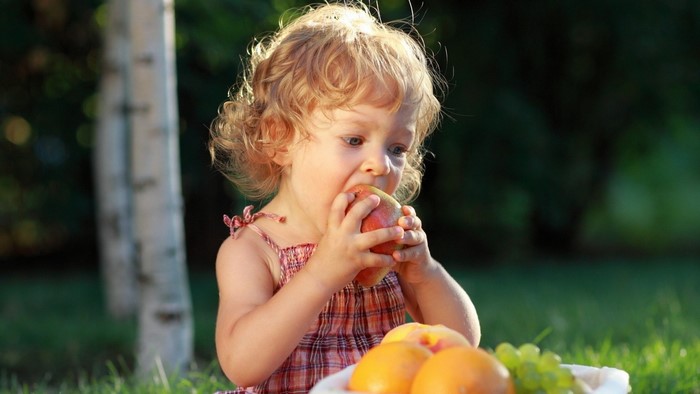 Toddler eating a mango in a park