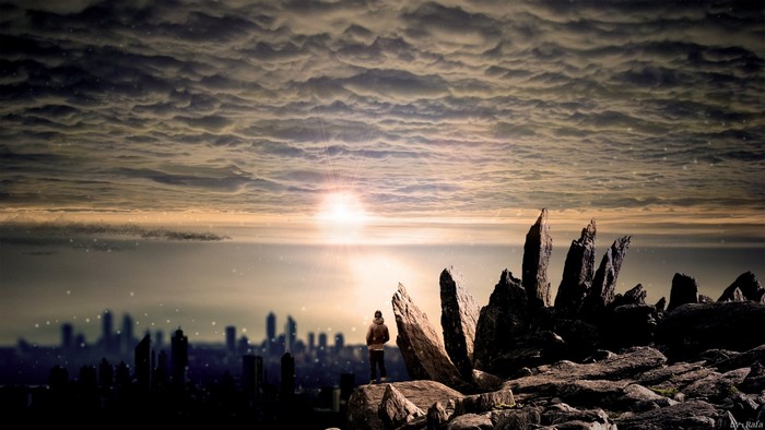 Man on rocks overlooking city at sunset