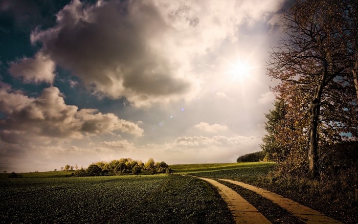 Autumn landscape with a dirt road and sunlit clouds