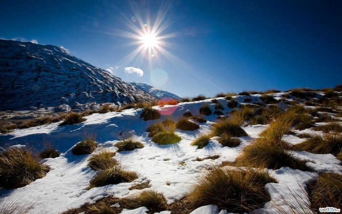 Sunlight over snowy mountain landscape with dry grass