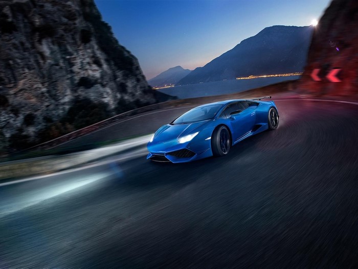 Blue Lamborghini Huracan driving on a winding road at dusk