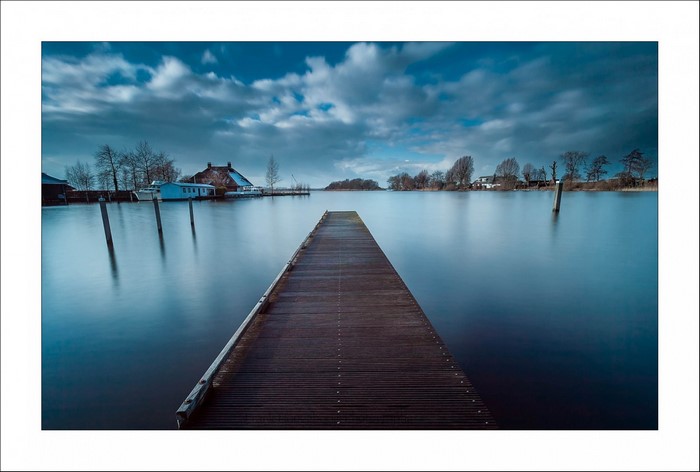 Wooden pier on a calm lake with houses and trees on the horizon