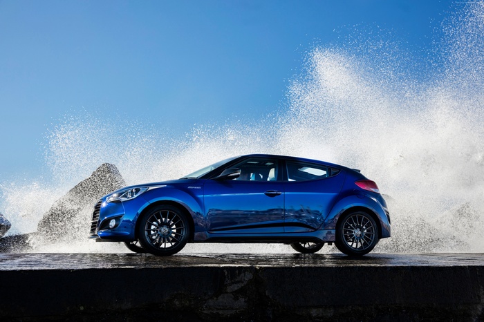 Blue Hyundai Veloster Turbo on a rocky shore with waves