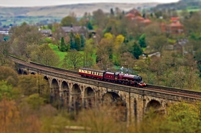 Steam train crossing a stone viaduct in a rural landscape