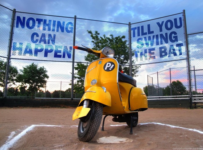 Yellow Vespa scooter on a baseball field with FLCL banner