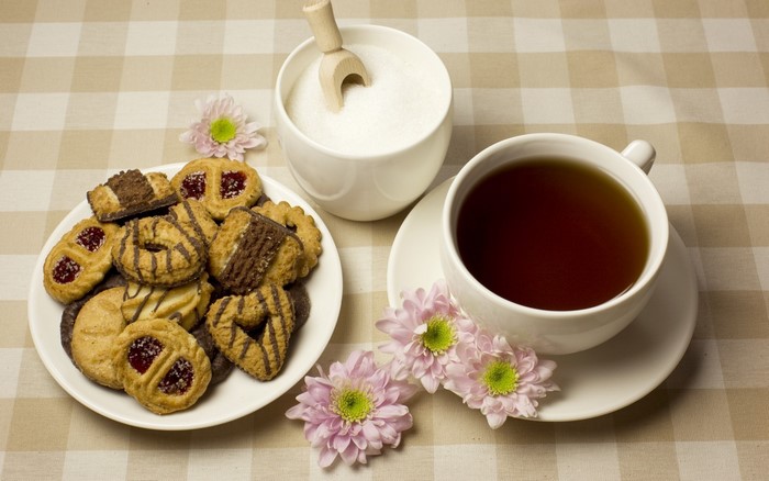 Tea, cookies, sugar, and flowers on a checkered tablecloth