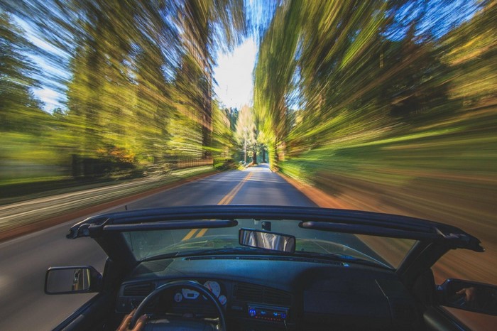 Driving a convertible on a tree-lined road with motion blur