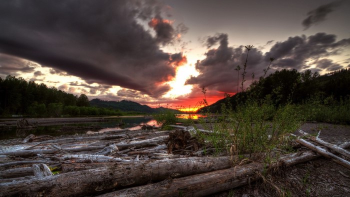 Sunset over a lake with driftwood and stormy clouds