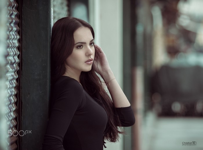 Woman with long brown hair leaning against a wall