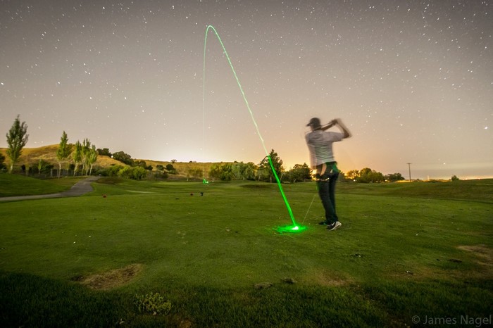 Golfer swings club with green light trail at night