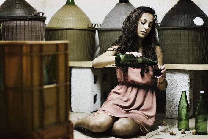 Woman pouring wine in a cellar with large carboys