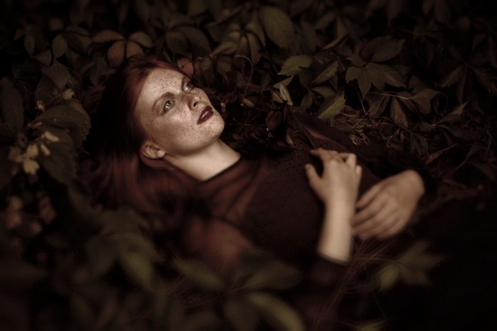 Woman with red hair and freckles lying in leaves